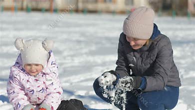 Mom and daughter have fun on the street in a beautiful winter snowy day, my mother throws snow at the girl, the girl