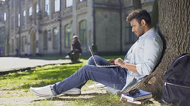 Multinational young man reading information on laptop under tree, surprised