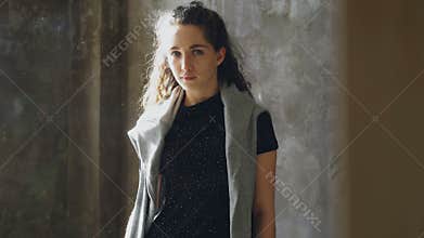 Portrait of attractive young girl standing still in and looking at camera. Dust flying around sunny room