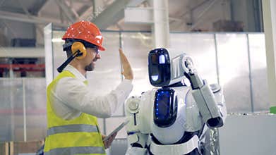 Human factory worker and an android give each other a hi-five at a factory facility.