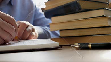 Man is writing in notepad and pile of books in library. Education and knowledge concept.
