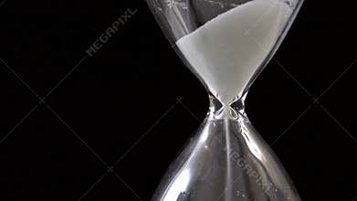 Detail of sand pouring in hourglass on black background, time passing concept