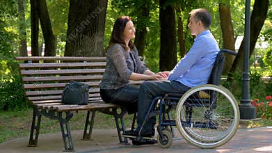 Young man on wheelchair talking with his wife in park