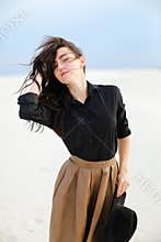 Young pretty woman wearing black blouse and brown skirt standing in white background and keeping hat.