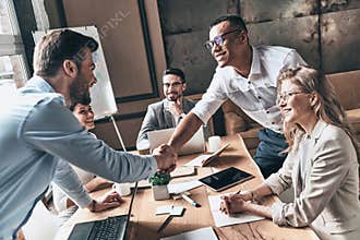 Welcome to our team! Top view of young modern men in smart casual wear shaking hands while working in the creative office