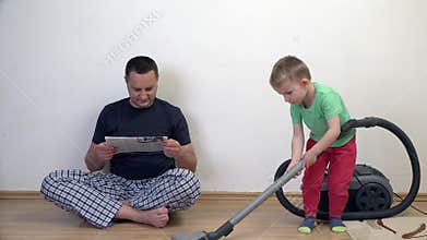 Man reads newspaper while kid is cleaning house with vacuum cleaner