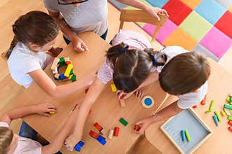 Preschool teacher with children playing with colorful wooden didactic toys at kindergarten