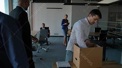 Young employee unpack box with docs and equipment. His colleagues walking near in modern office