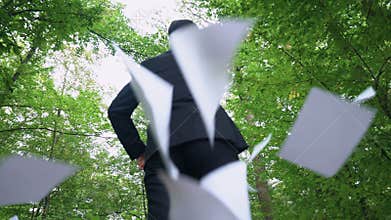 Businessman walking in forest and throwing away all papers, enjoying freedom