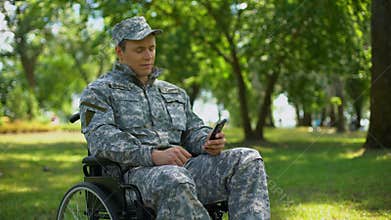 Disabled military man scrolling smartphone photos, rest in city park, nostalgia
