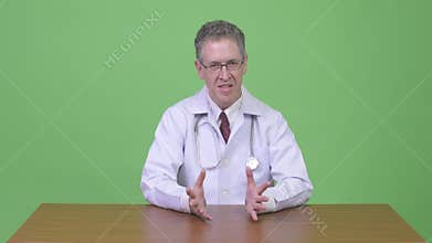 Mature man doctor explaining something against wooden table