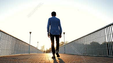 Young handsome business man or student walking alone on empty bridge or street. Back view. Traveling the world. Success