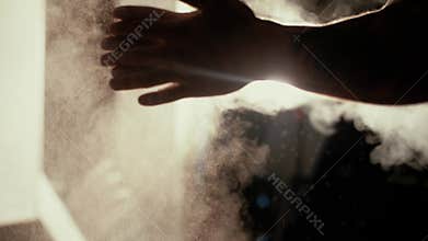 Strong muscular bodybuilder clapping hands with chalk powder before training with a dumbbell in a dark room.