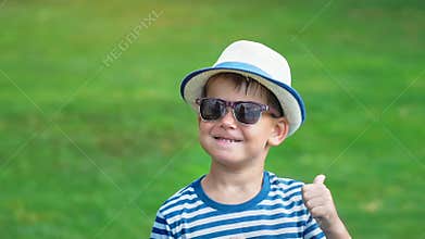 Portrait happy smiling little boy in sunglasses and hat having fun dancing in summer park