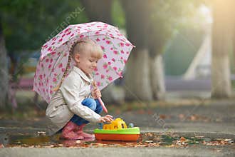 A girl playing in the puddle with the boat after rain
