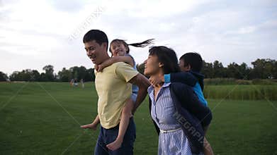 Asian parents giving children piggyback ride in park