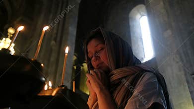 Woman in a headscarf praying before an icon in the Orthodox Catholic Church