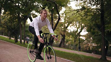 Happy, smiling young man in white shirt have a bicycle ride by riding path in green city park. Riding his trekking bike