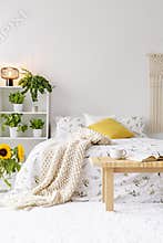 Sunny spring bedroom interior with green plants beside a bed dressed in eco cotton linen. Yellow accents