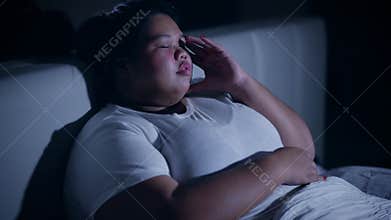 Obese woman with insomnia sitting on bed