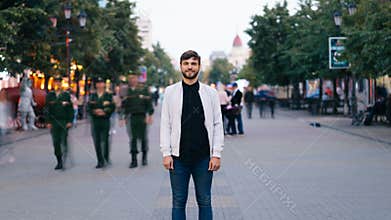 Zoom in time-lapse of attractive young guy businessman looking at camera standing in the street in city center then