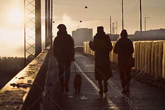 A walk with the dog and friends. Silhouettes of walking people and dog on a bridge in winter sunset.