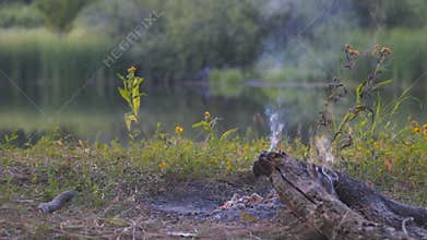 An extinct bonfire in the camp by the lake. Light smoke from coals and an extinct fire