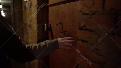 the girl's hand runs her fingers along a brick wall in a creepy basement a terrible hopeless place