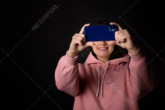 Cute young brunette in a pink hoodie uses a smartphone and laughs, communication without borders,