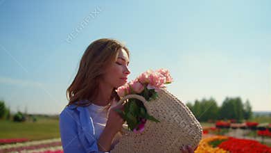Relaxed woman with basket of flowers standing in beautiful blooming tulip field.