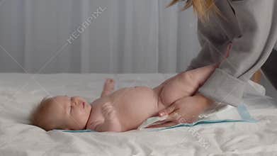 Unrecognizable Mother Changing Diaper To Her Cute Newborn Baby Lying On Bed