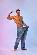 Young man showing how much weight he lost with big jeans. Fat to fit concept. Fitness poster