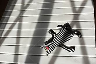 Conceptual. Lost childhood, war, death. Abandoned children's soft toy on white wooden floor with cross window shadow