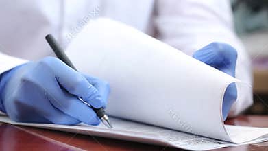 A doctor in rubber gloves fills out documents with a pen. The doctor works with documents. Working during a pandemic