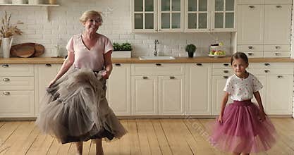 Happy older grandmother dancing with small child girl in kitchen.