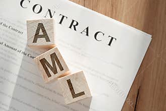 Three wooden cubes with the letters AML anti-money laundering on the contract lying on wooden table
