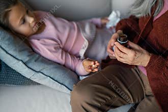 Grandmother taking care of her ill grandchild lying on sofa