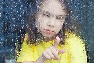 a little girl behind a rain-splattered window