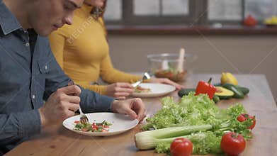 The husband and wife are sitting in the kitchen at the table, couple eating vegetable salad