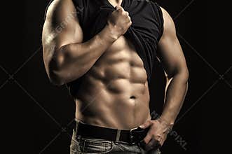 Sexy strong young man with muscular body in blue jeans with shirt on shoulder standing posing in studio on black