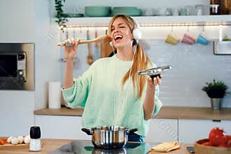 Beautiful young woman cooking while singing and listening music with headphones in the kitchen at home