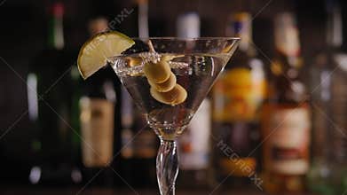 Close-up of a Martini glass with olives and lemon slowly rotating on the bar.