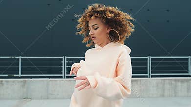 Fashionable funky curly afro dancer woman in sportswear is performing outdoor street dancing motion. Joyful summer