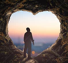 Silhouette of Man Gazing at City Lights from Heart Shaped Cave Opening at Twilight