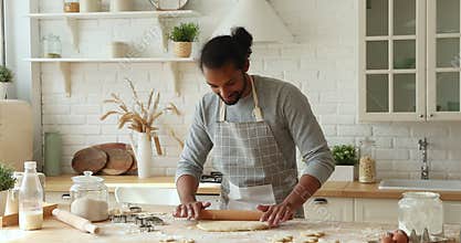 African man wear apron rolls out the dough for baking