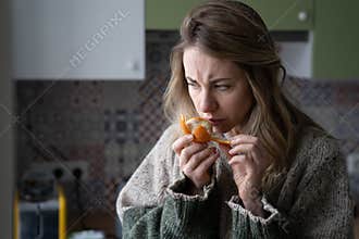 Sick woman trying to sense smell of fresh tangerine orange, has symptoms of Covid-19, corona virus