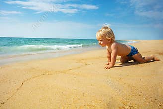Cute boy crawl on the sand beach near sea waves