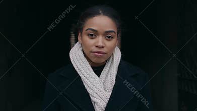 Tracking shot outdoor portrait of young african american woman standing outdoors in warm coat