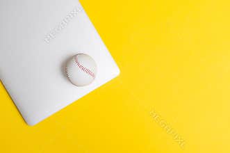 Baseball ball and grey laptop on yellow background. Online workout concept. Top view, space for your text