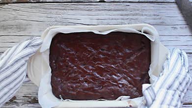 Woman`s hands wearing oven mitts and setting down a dish of freshly baked chocolate brownies.